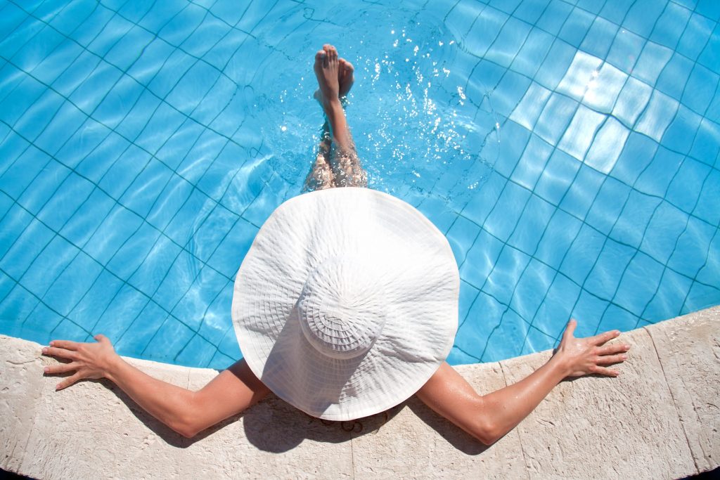 A photo that is looking down ontop of a woman lounging in a pool with a large white sun hate on.