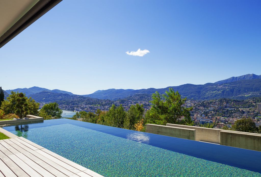 A beautiful infinity edge swimming pool that is overlooking a mountain landscape and blue sky with a single cloud.
