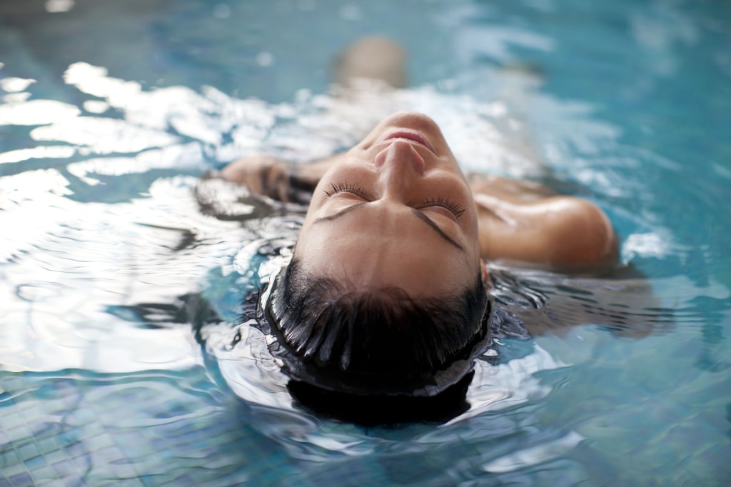 A close up photo of a young woman with brown hair floating on her back in a swiming pool.
