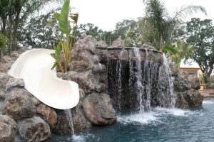 A picture that focuses on a waterfall inspired by natural rock design and slide leading to a swimming pool.