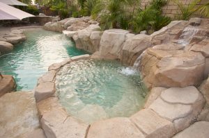 A close up of a hot tub inspired by a natural spring with a pool in the background.