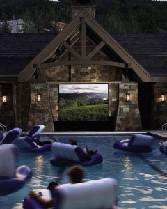 Many people on pool floats watching a movie in a backyard.
