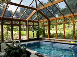 An elegant and luxurious wooden swimming pool enclosure surrounded by a green landscape.