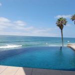 Amazing infinity edge pool over looking the ocean with palm trees in foreground.