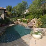 freeform pool with a rock waterfall water feature in a backyard.