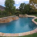 Freeform pool with decorative coping and raised rock spa in residential backyard featuring waterfall.