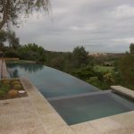 Infinity edge pool with spa overlooking cloudy landscape.